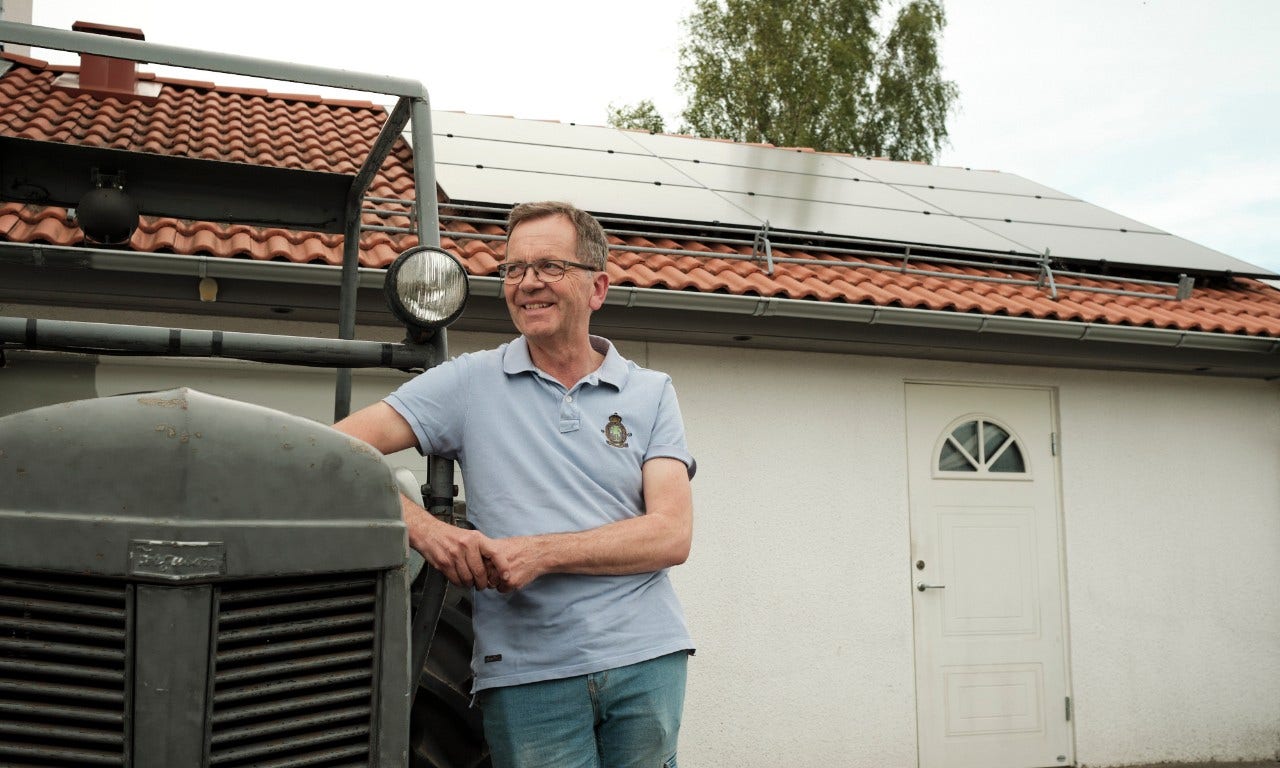 Man som lutar sig mot en traktor, frmför ett hus med solpaneler