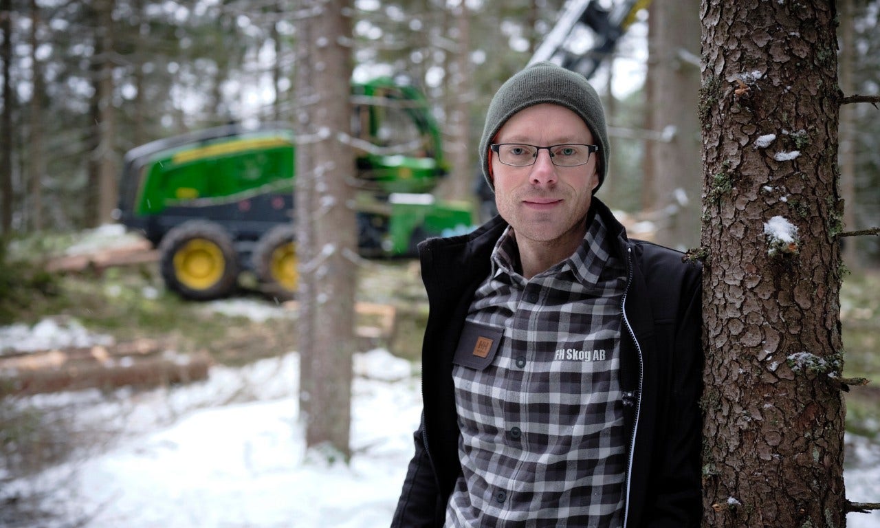 Skogsarbetare som lutar sig mot ett träd, framför sin skogsmaskin