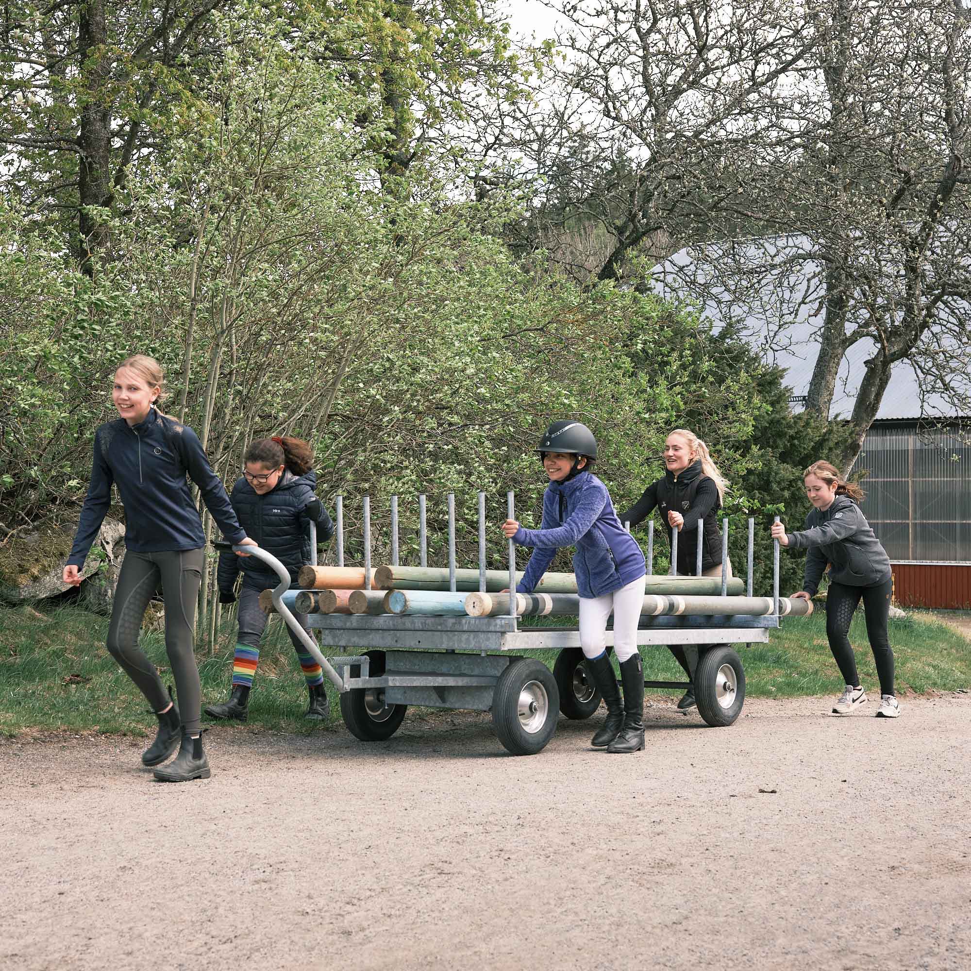 Fem ryttare som drar en vagn med bommar till hästhinder