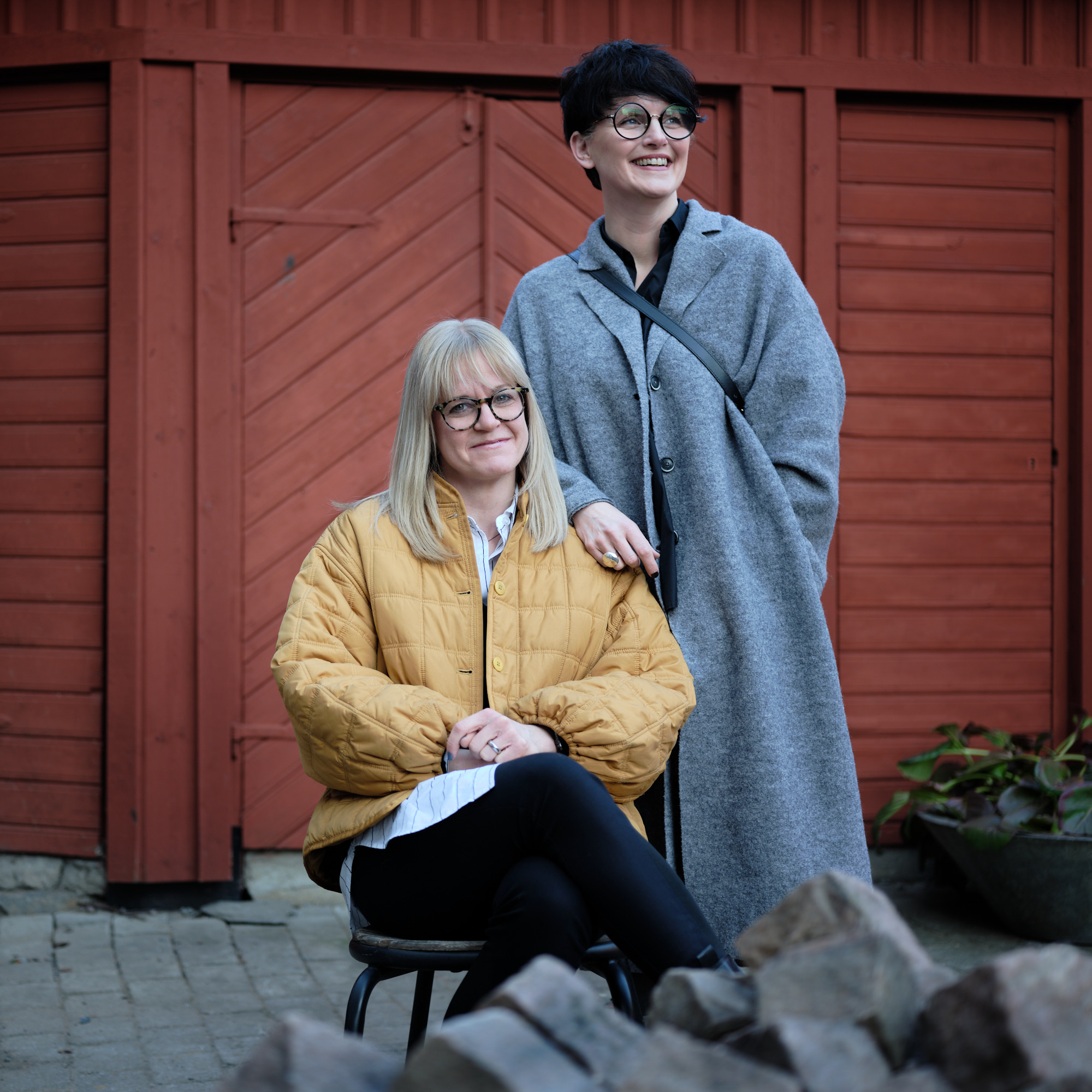 Två leende kollegor framför en röd vägg