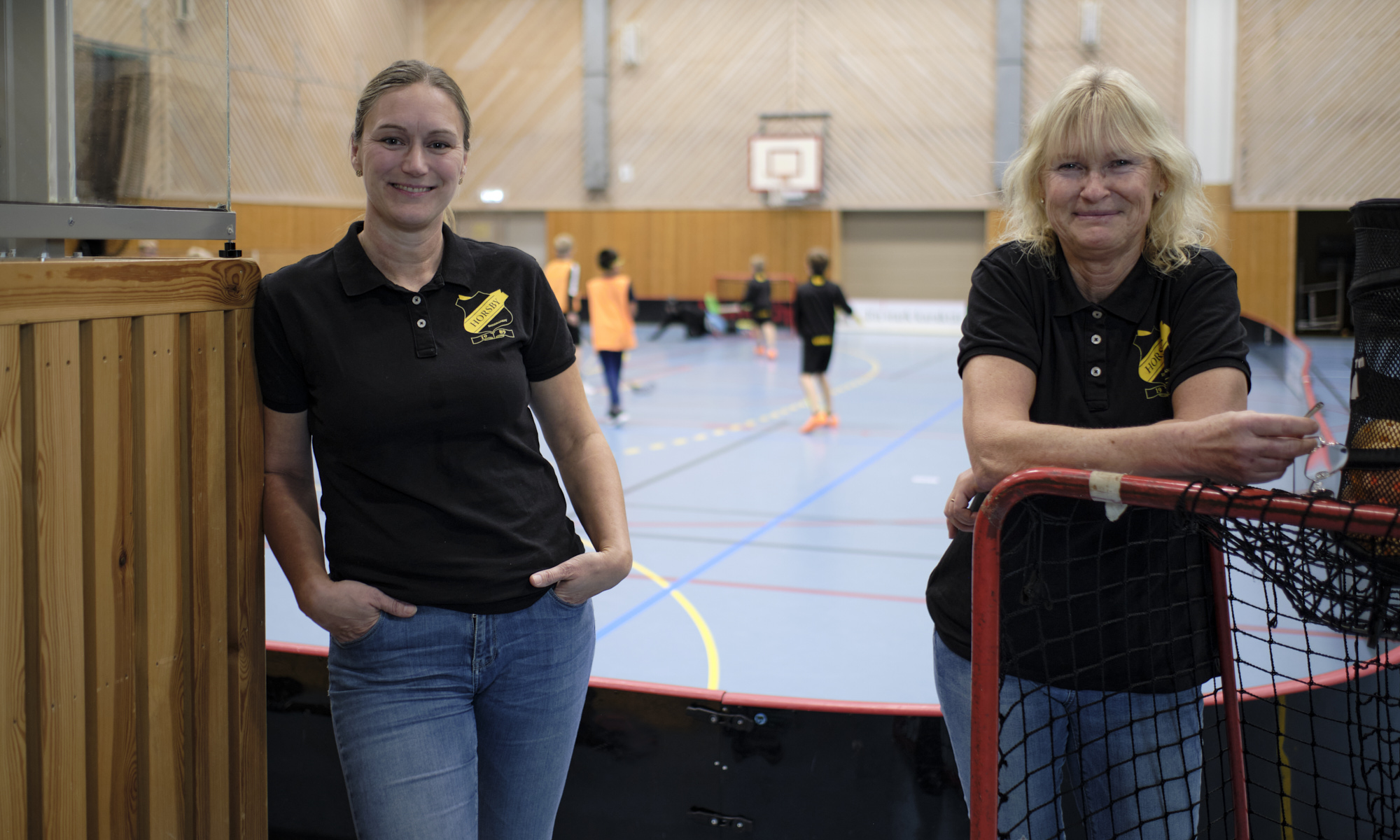Två leende kvinnor vid en innebandyplan