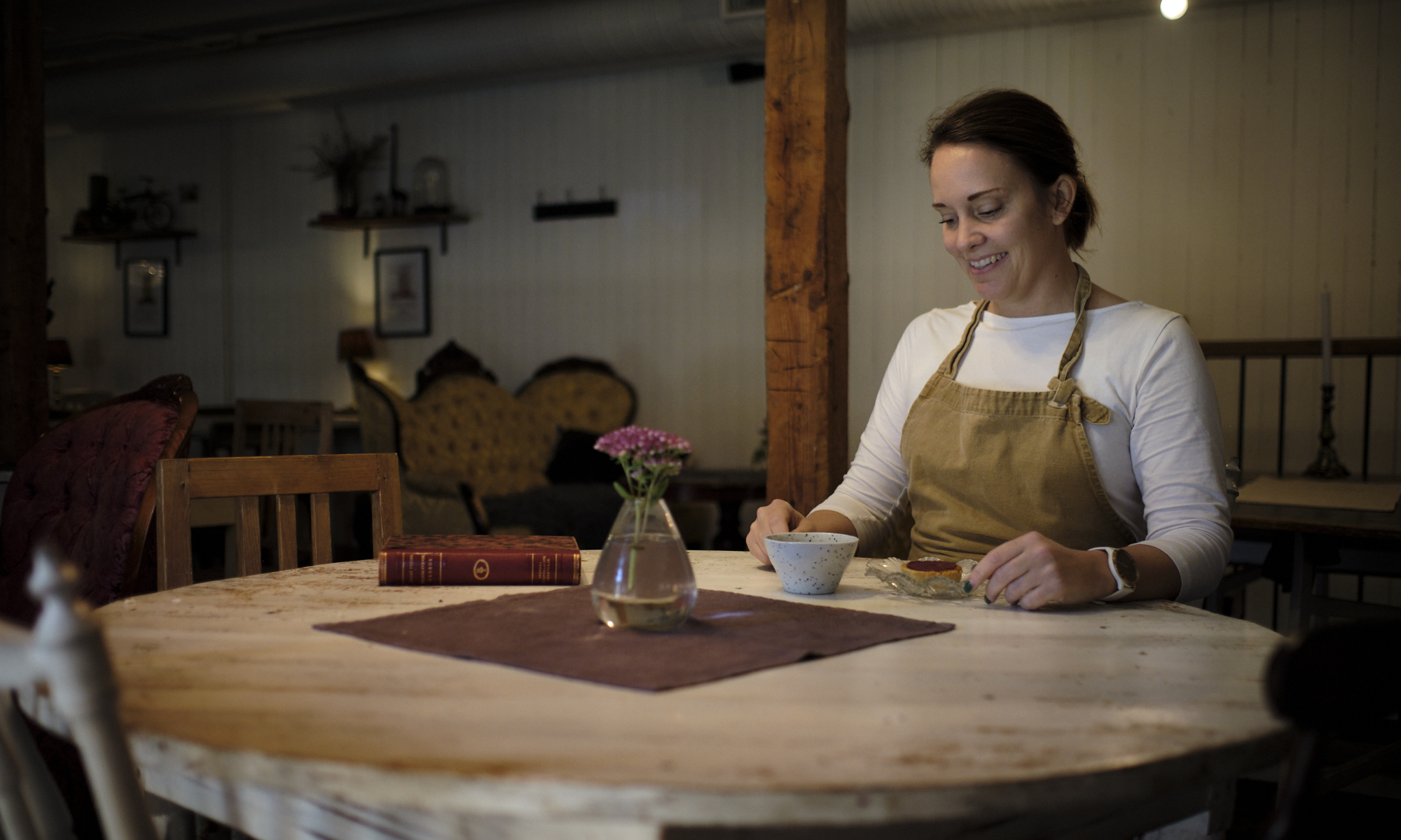 En leende kvinna vid ett bord med en kaka och kopp kaffe