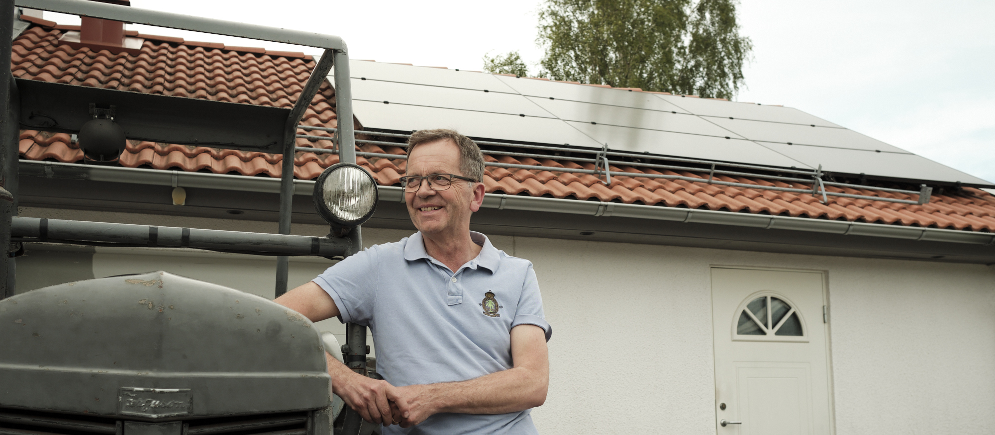 Leende man håller i en solpanel framför ett hus